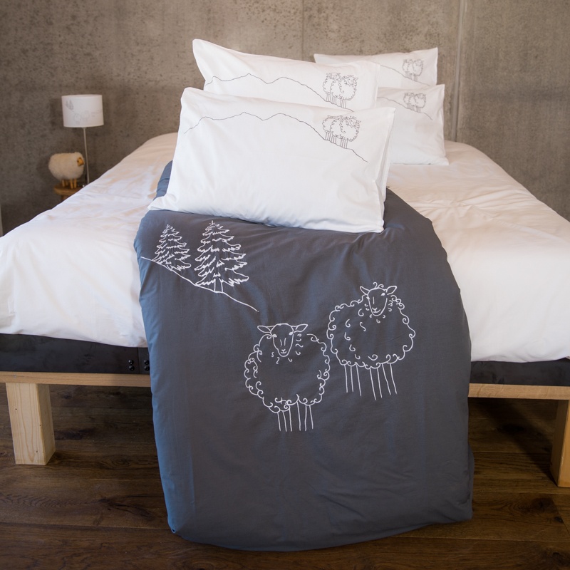 Grey cotton percale mountain duvet cover embroidered with white sheep in a contemporary bedroom.