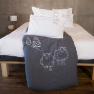 Grey cotton percale mountain duvet cover embroidered with white sheep in a contemporary bedroom.