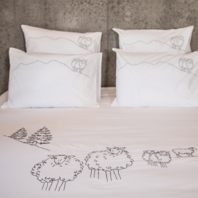 White mountain bedding set with duvet cover and four pillows with embroidered sheep patterns.