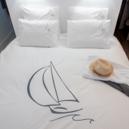 White pillowcase embroidered with a grey sailboat and its matching duvet cover on a bed.