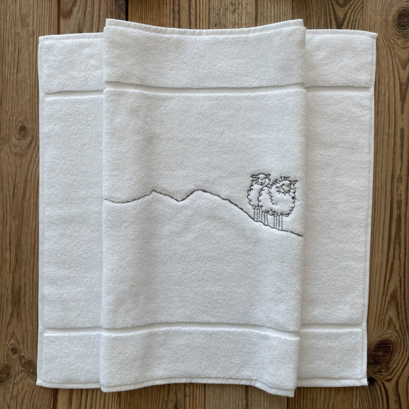White mountain bath mat with grey sheep embroidery.