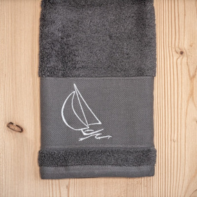 Serviette de toilette bord de mer grise brodée d'un motif voilier blanc.