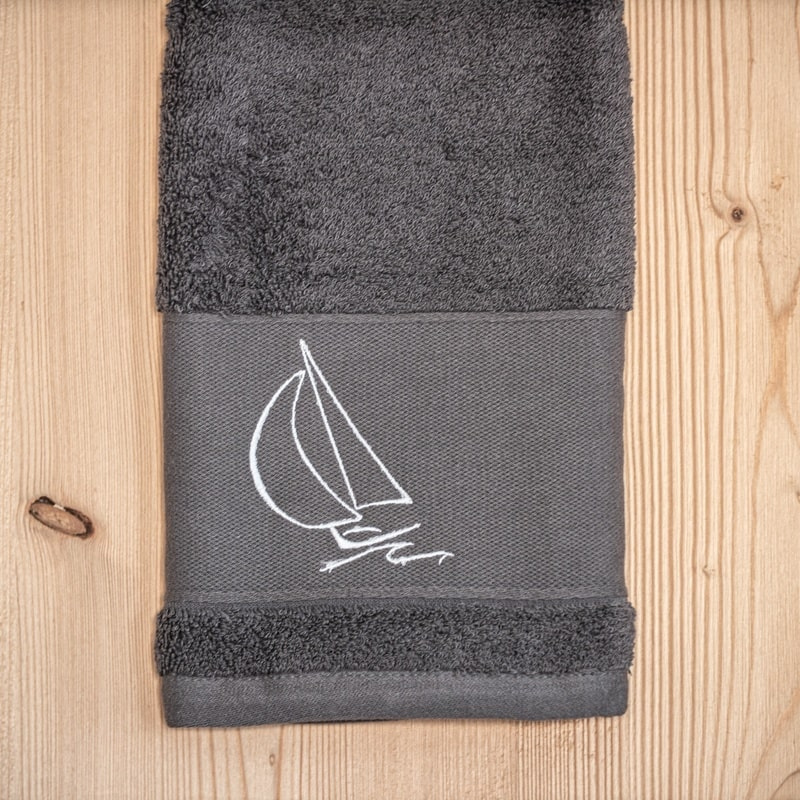 Serviette de toilette bord de mer grise brodée d'un motif voilier blanc.