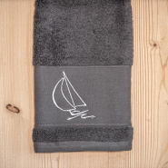Serviette de toilette bord de mer grise brodée d'un motif voilier blanc.