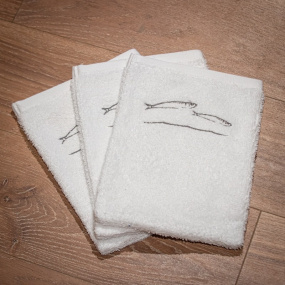 Trois gants de toilette blancs style bord de mer brodés de motifs de poissons gris.