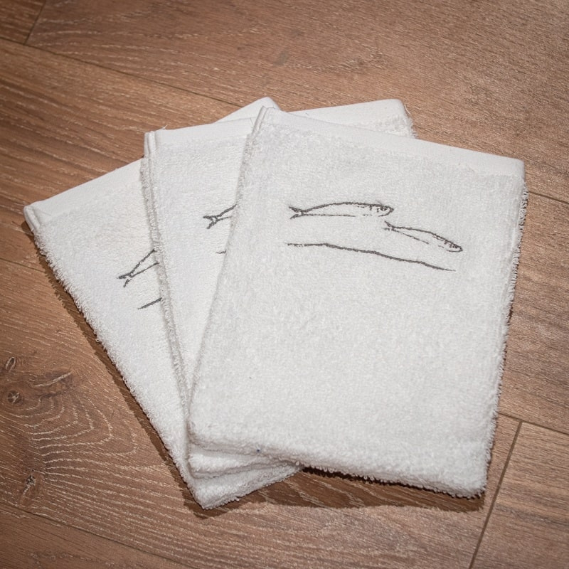 Trois gants de toilette blancs style bord de mer brodés de motifs de poissons gris.