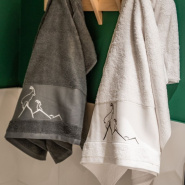 Toalla de baño gris y blanca con motivos de montaña, bordada con un íbice.