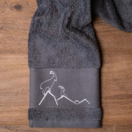 Toalla de baño gris con motivos de montaña, bordada con un ibice blanco.