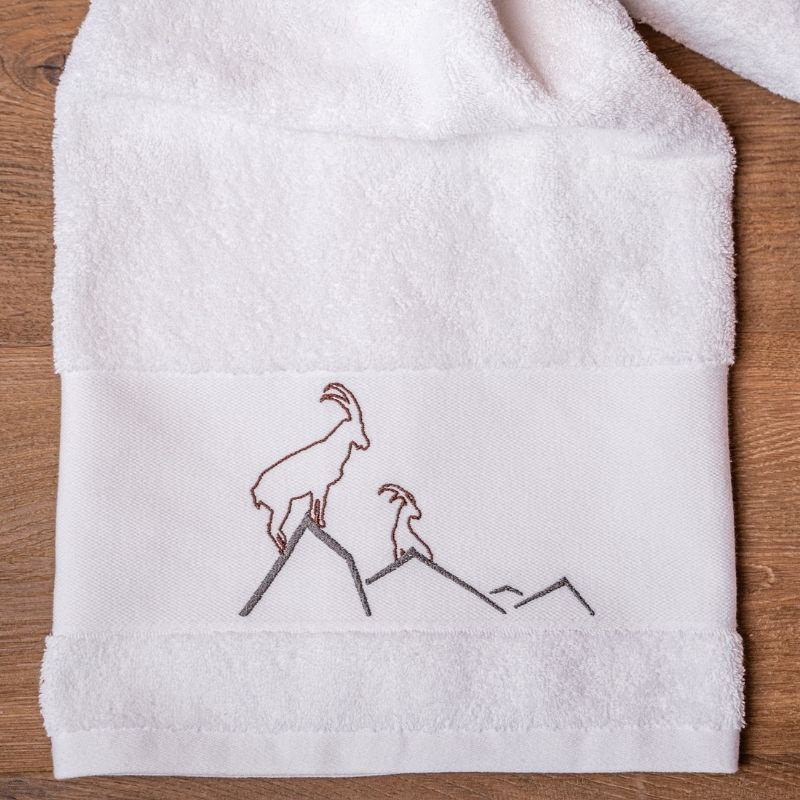Toalla de baño blanca con motivos de montaña, bordada con un diseño de íbice.