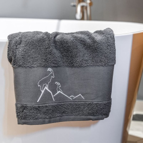 Toalla de baño gris con un bordado de un íbice gris claro en el borde de una bañera.