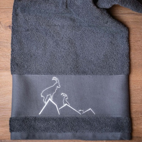 Toalla de baño gris con motivos de montaña, bordada con un íbice blanco.