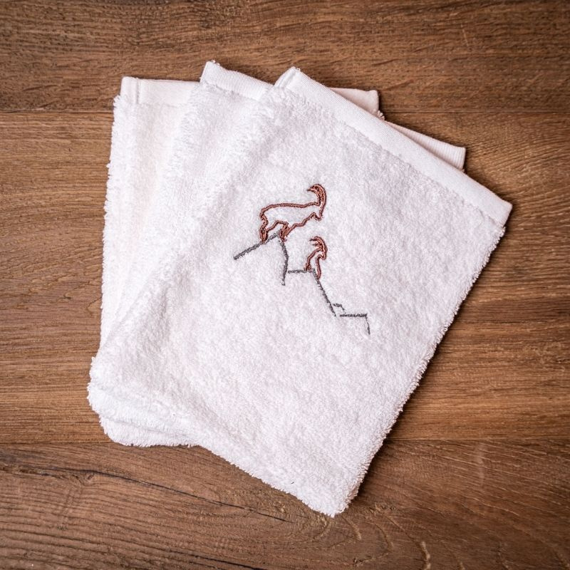 Three white mountain washcloths embroidered with an ibex motif.