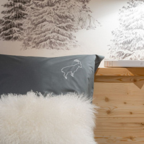 Grey cotton percale pillowcase with an embroidered white ibex, set in a contemporary mountain bedroom.