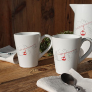 Due mug bianchi in terracotta e una brocca coordinata con motivo di funivia rossa stile montagna.