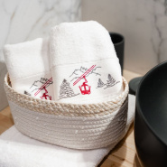 Dos toallas de baño blancas de estilo montañés con un bordado de un teleférico rojo en una cesta de baño