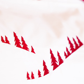 Detalle del bordado de bosque de abetos rojo en la funda de percal de algodón blanco.