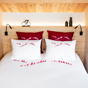 Funda nórdica de montaña blanca bordada con un bosque de abetos rojo en un dormitorio de chalet.