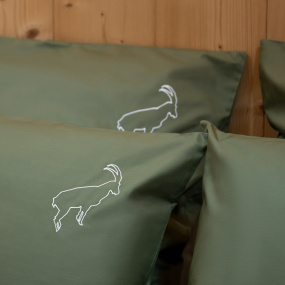 Focus on the ibex embroidery of the green cotton percale mountain-themed pillowcase.