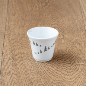 Tazza da caffè in maiolica bianca con motivi di abeti grigi.