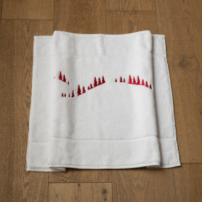 Alfombra de baño blanca con motivos de montaña, bordada con un bosque de abetos rojos.