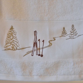 Toalla de baño blanca con motivos de montaña, bordada con un diseño de huellas de esquí en marrón y beige.