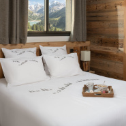 Housse de couette montagne en percale blanche brodée d'une forêt de sapins gris placée dans une chambre de chalet.