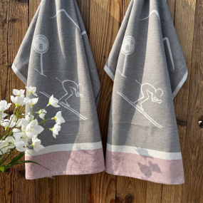 Two mountain kitchen towels with a design of a skier going down the slopes.