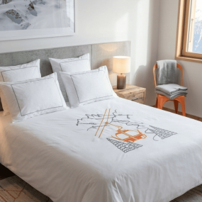 White cotton percale mountain duvet cover with orange cable car embroidery in a contemporary bedroom.