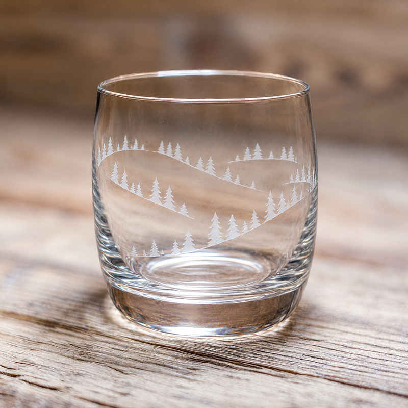 Mountain water glass with fir trees and snowy hills design, on a rustic wooden table