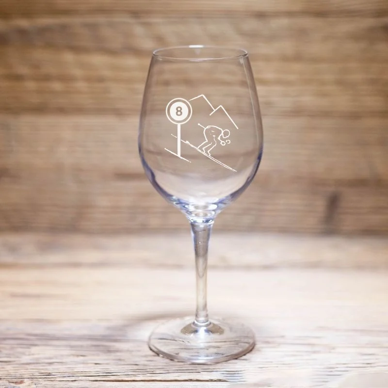 Mountain wine glass with Schuss skier and piste sign design, on a wooden table.