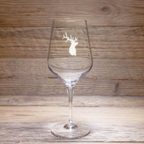 A mountain-themed wine tasting glass with a deer design, resting on a rustic wooden table