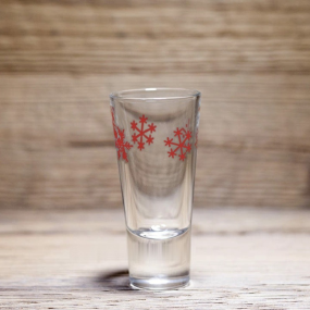 Verre à liqueur montagne à motif flocons de neige rouges, posé sur une table en bois