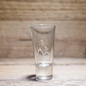 Verre à liqueur montagne à motif deux bouquetins sur les sommets, posé sur une table en bois