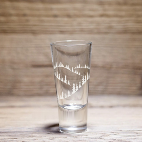 Verre à liqueur montagne à motif sapins et collines enneigées, posé sur une table en bois